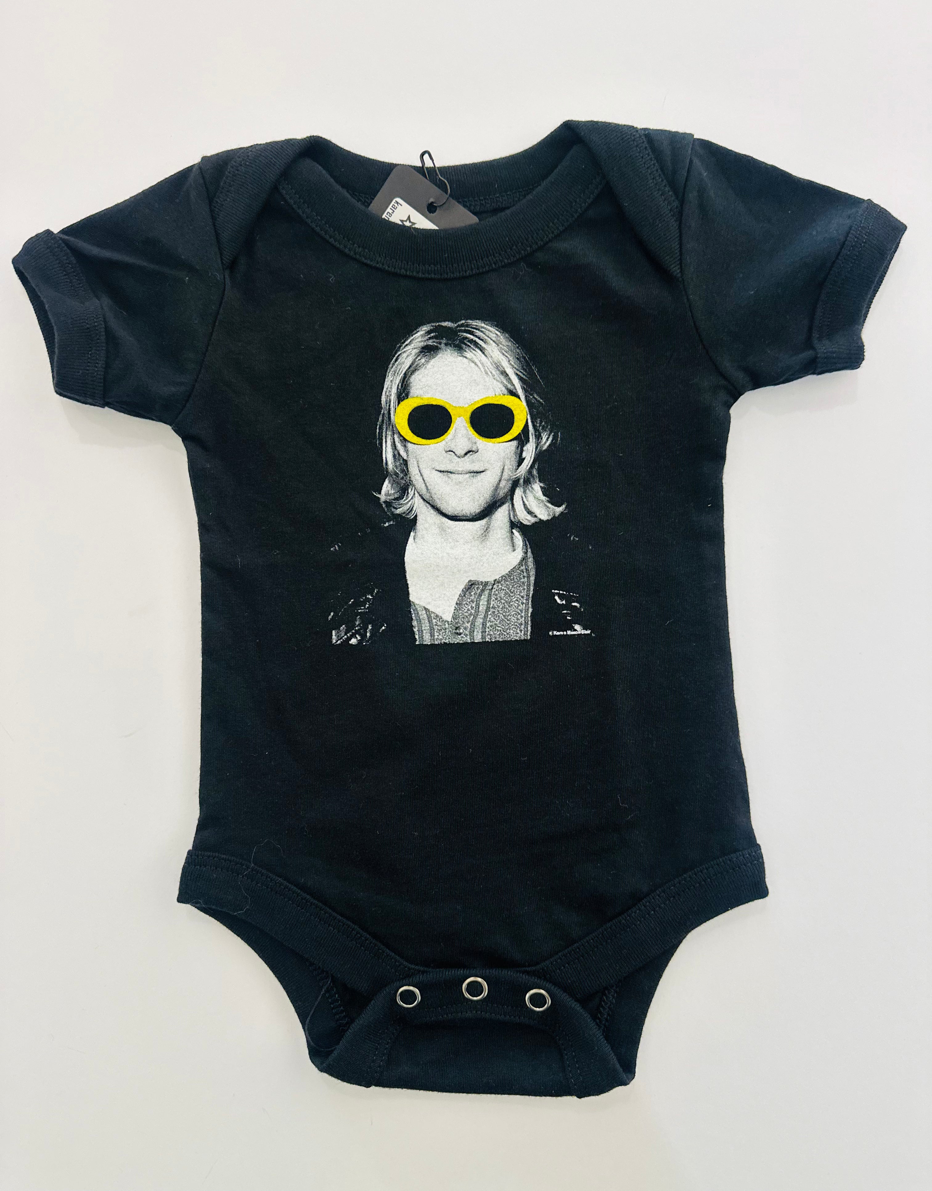 The Kurt Cobain baby onesie features a black-and-white portrait of the musician from Nirvana wearing his iconic sunglasses in yellow. Made of cotton with limited stock available. Photo by the Seattle grunge music scene photographer Karen Mason Blair, available at Grunge Mart.